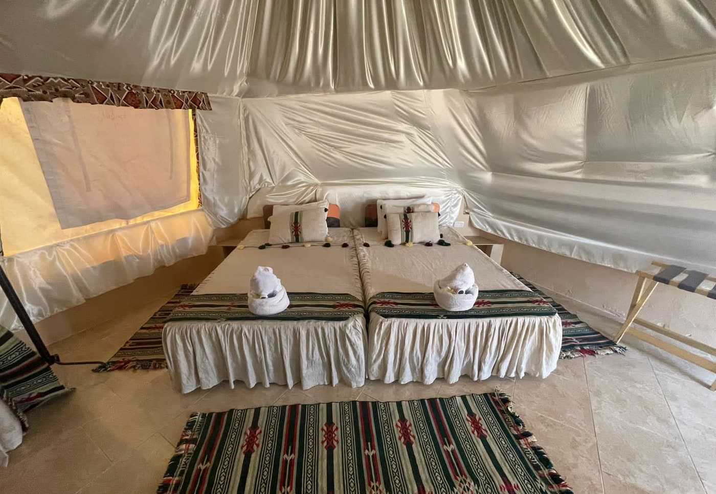 Twin beds made up inside a canvas tent, rugs on the floor