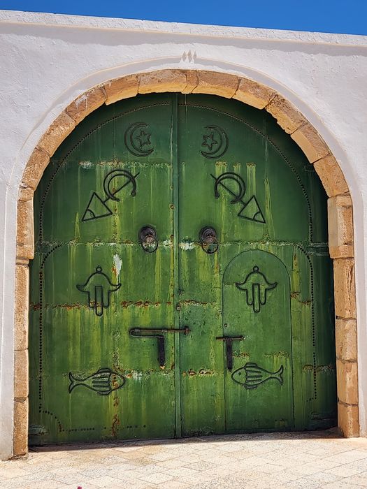 A green door marked with hamsas and fish on Djerba