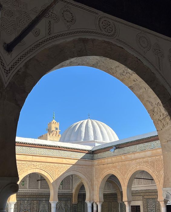 A white dome and tiled courtyard seen through a carved arch